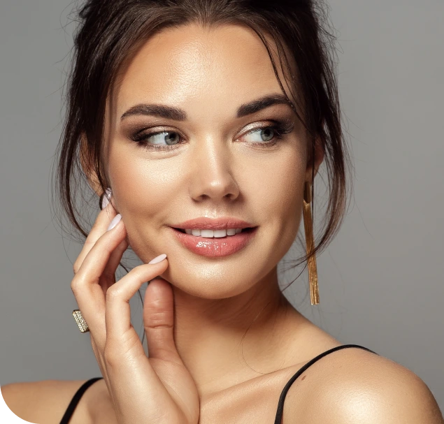 Woman with clear skin touching her cheek and smiling toward camera against neutral background